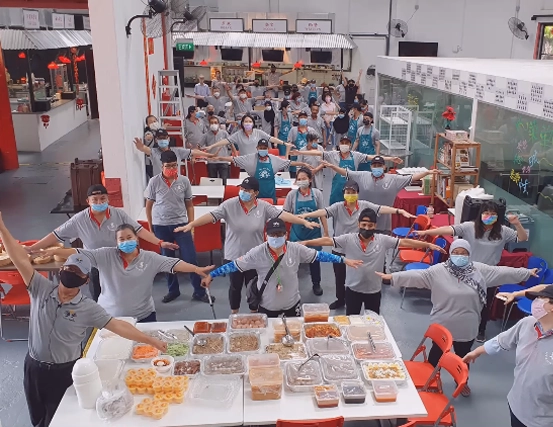 Photo of a large group of people wearing medical masks and grey t-shirts in a warehouse. They stand spaced out with their arms extended. Text reads, Dignity Restored with Project Dignity Mr. Koh Seng Choon Executive Director In Singapore and Hong Kong.