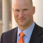 Photo is a headshot of a man in a blue suit with an orange tie. Headline states, Interview with Charlie Hammerman.