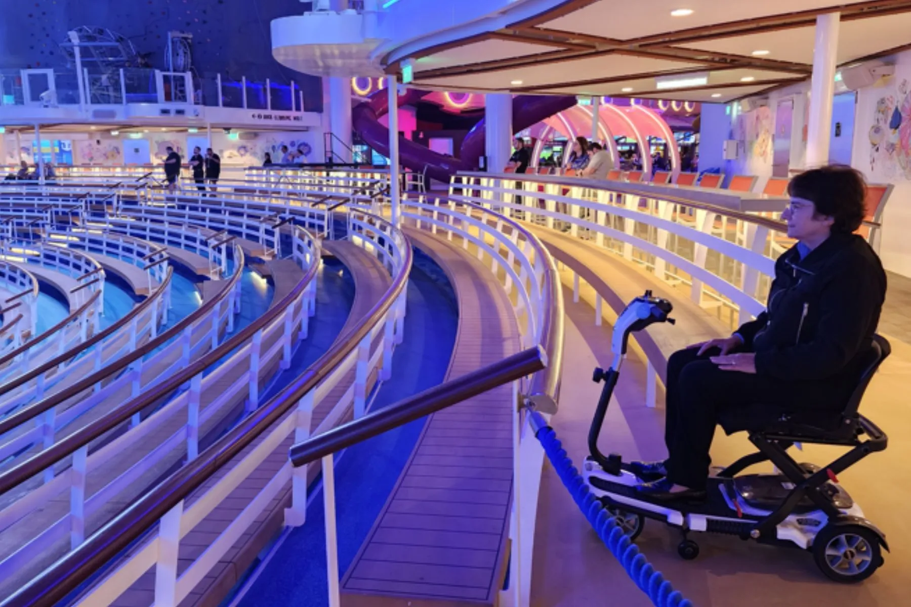 A woman sits in a power scooter on the upper level of an outdoor theater on a deck of a cruise ship. Cruising on Wonder of the Seas by Rosemarie Rossetti, PhD. Read More.