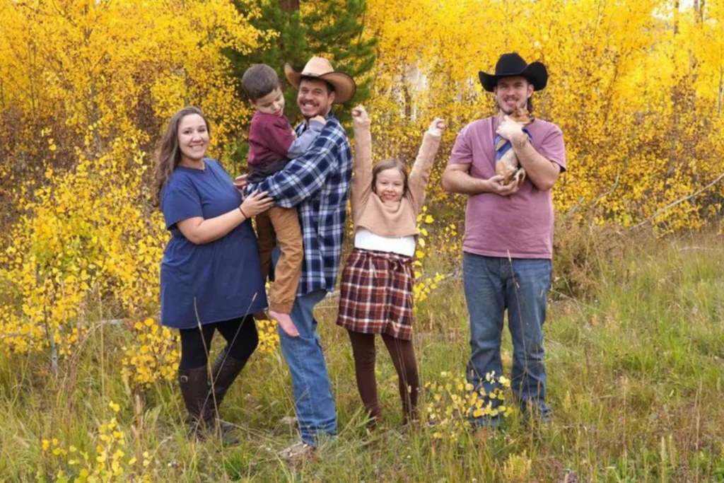 A group of smiling people stand in a forest of yellow foliage and tall grass. One man wears a black cowboy hat and holds a chihuahua. A girl punches the air with her arms. A man in a tan cowboy hat holds a boy in his arms as a very pregnant woman rests a hand on his arm. The headline reads, A happy life, full of adventure. Accessible Journeys' (AJ) guest editor. . . Read More.