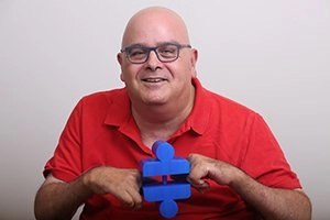 A smiling man in a bright red golf-shirt holds bright blue blocks between his hands. Headline reads, Yuval Wagner, Founder & Chairman of Access Israel.