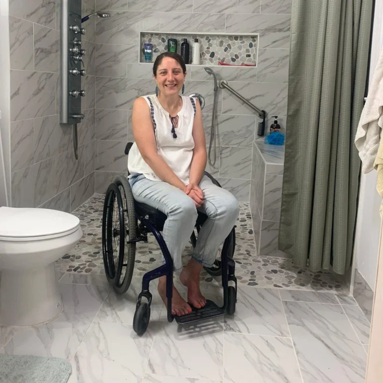 A woman in a wheelchair is seated in a bathroom, highlighting accessibility features in the space.