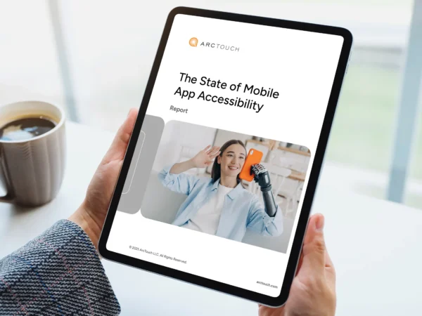 ArcTouch SOMAA Report Cover A person holding a tablet displaying a report titled "The State of Mobile App Accessibility," with a coffee mug nearby.
