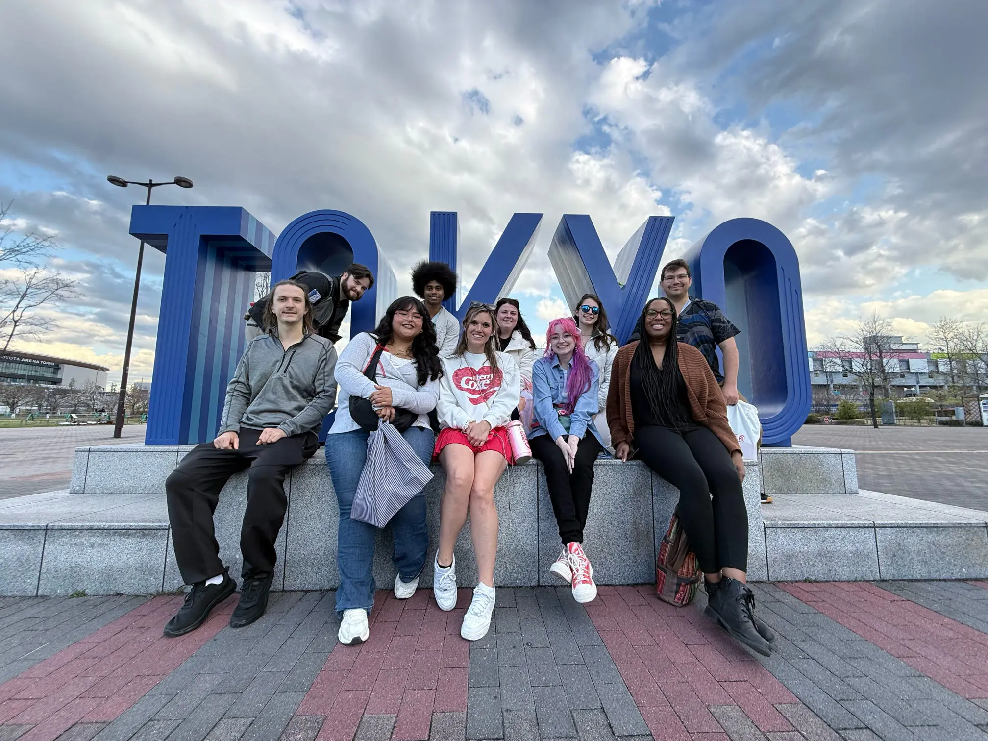 Group of diverse people posing in front of a large, stylized "TOKYO" sign.