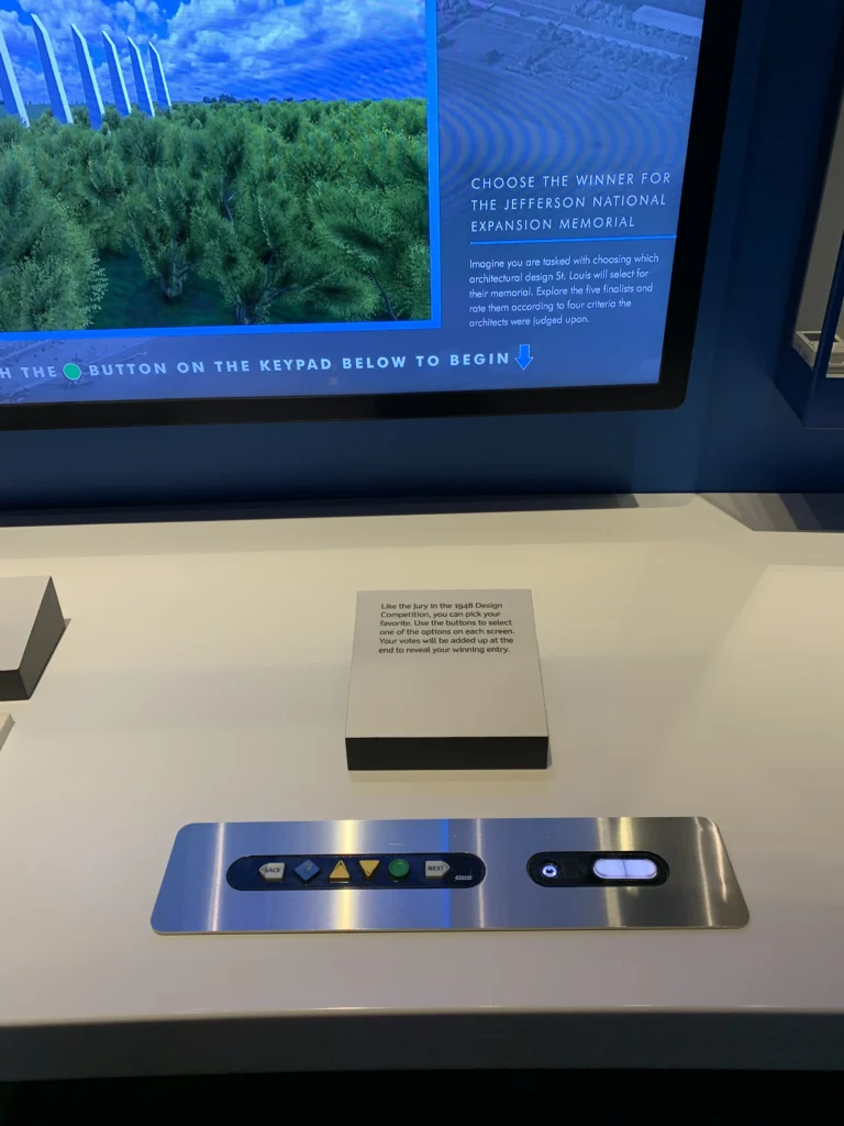 Interactive exhibit panel with keypad and display screen, inviting users to vote for the Jefferson National Expansion Memorial winner. Instructions and information are visible above the keypad.