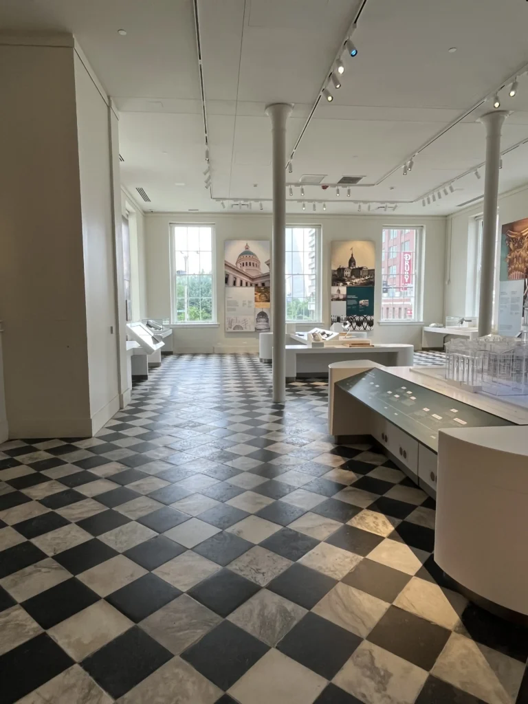 Interior of a museum with a black and white checkered floor, showcasing exhibits and large windows allowing natural light.