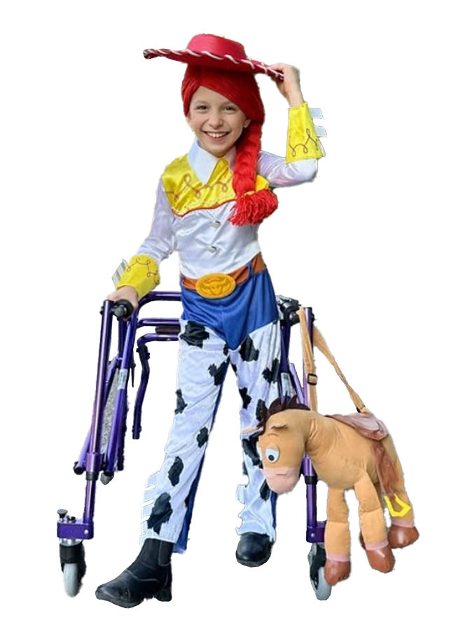 A child dressed as a cowboy, featuring a yellow and white shirt, blue pants with cow prints, and a red hat, using a walker while holding a toy horse.