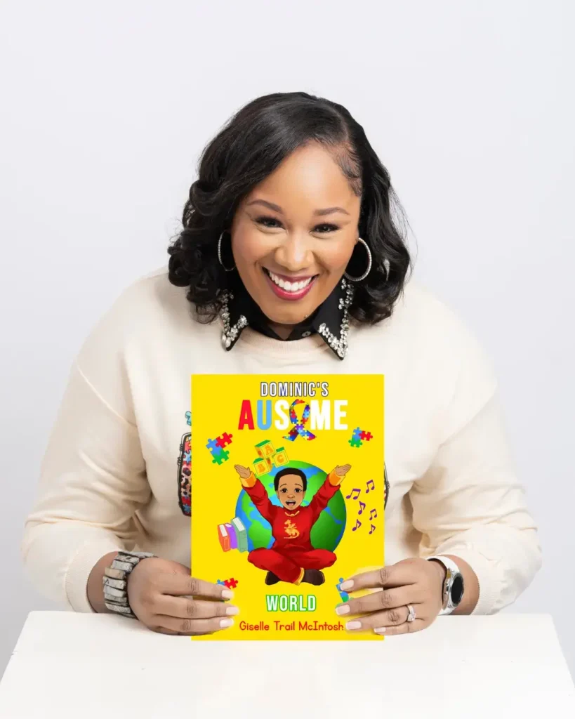 Close-up portrait of author Giselle Trail McIntosh smiling and holding her children’s book, Dominic's Ausome World, which features a colorful illustration of a boy on the cover.