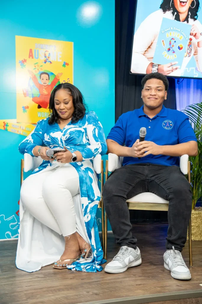 Author Giselle Trail McIntosh and her son Xachri-Kyle sitting on stage with microphones during a panel discussion about the creative process of the book Dominic's Ausome World at the Autism Trails brand launch.