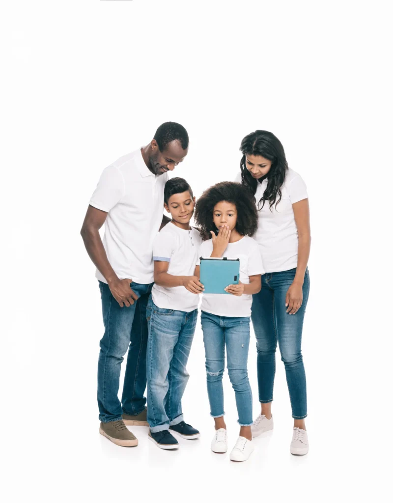 A family of four—a father, mother, son, and daughter—standing together against a solid white background. They are all dressed in matching white polo shirts and blue jeans. The two children are in the center, holding a blue tablet and looking at the screen with expressions of surprise and curiosity, while the parents lean in from either side, smiling warmly as they watch.