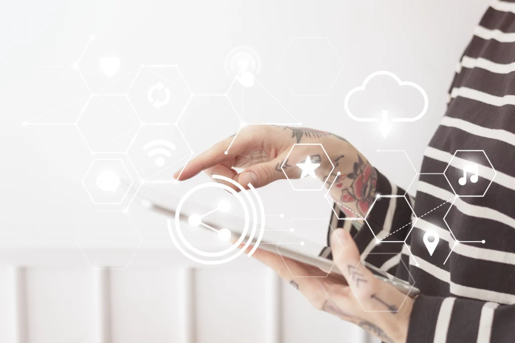 A close-up shot of a person with tattooed arms wearing a striped shirt, holding a digital tablet. Overlaid on the image are white, glowing digital icons inside hexagonal shapes, representing concepts like sharing, cloud syncing, Wi-Fi, and music.