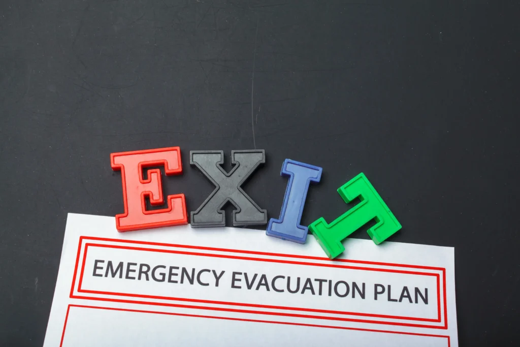Colorful block letters spelling "EXIT" resting on a white document titled "EMERGENCY EVACUATION PLAN" in bold black text, set against a dark background.