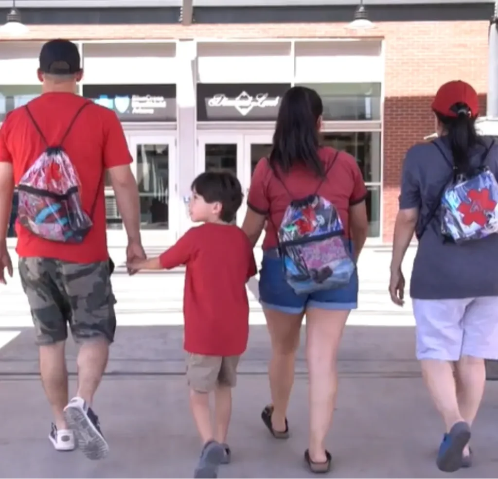 A family of four walks toward an entrance at a Diamondbacks baseball game, wearing red shirts and clear drawstring bags featuring the Arizona Diamondbacks logo.