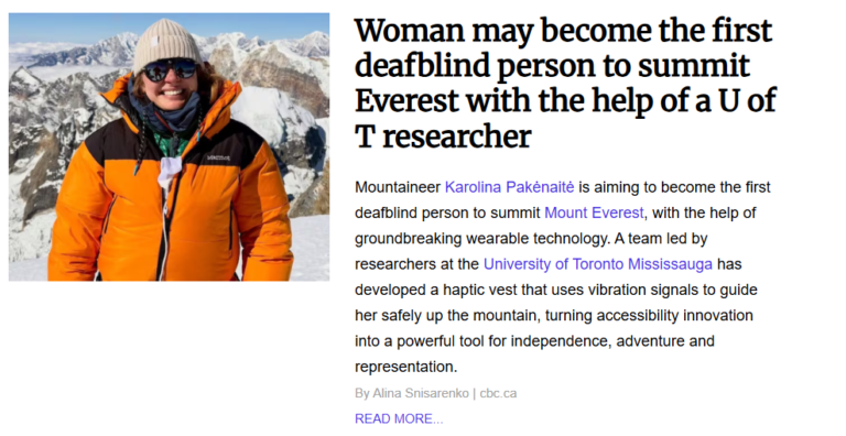 Mountaineer Karolina Pakėnaitė smiling in an orange and black winter jacket and beanie with snow-capped Himalayan mountains in the background.